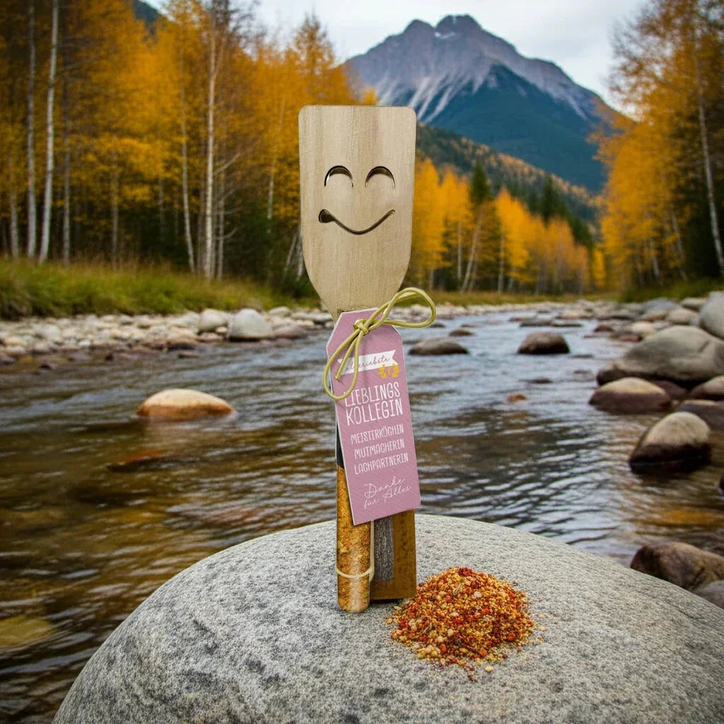 Lustige Holzspatel mit Geschenkgewürzen und Etikett 'Lieblingskollegin' auf Stein in Naturkulisse, feinkostgourmet