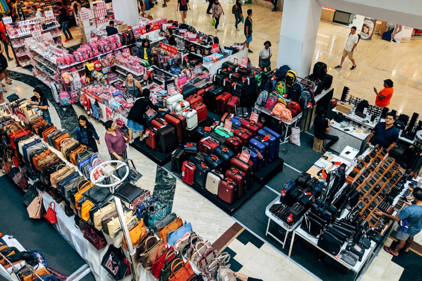 Buntes Koffer- und Taschenangebot in einem Einkaufszentrum, Menschen beim Stöbern.